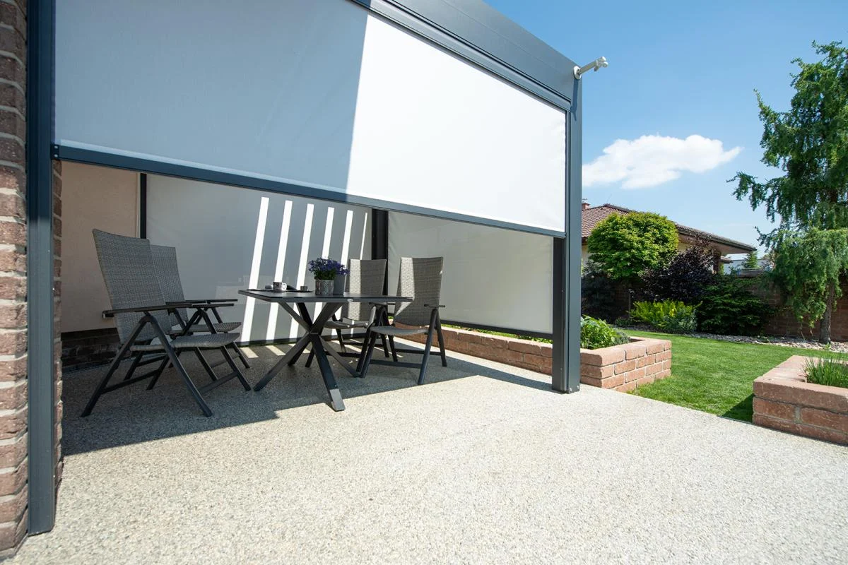 Außenterrasse mit Tisch, Stühlen und einem weißen Sonnenschirm, neben einem grünen Garten. Außenterrasse mit Tisch, Stühlen und einem weißen Sonnenschirm, neben einem grünen Garten.