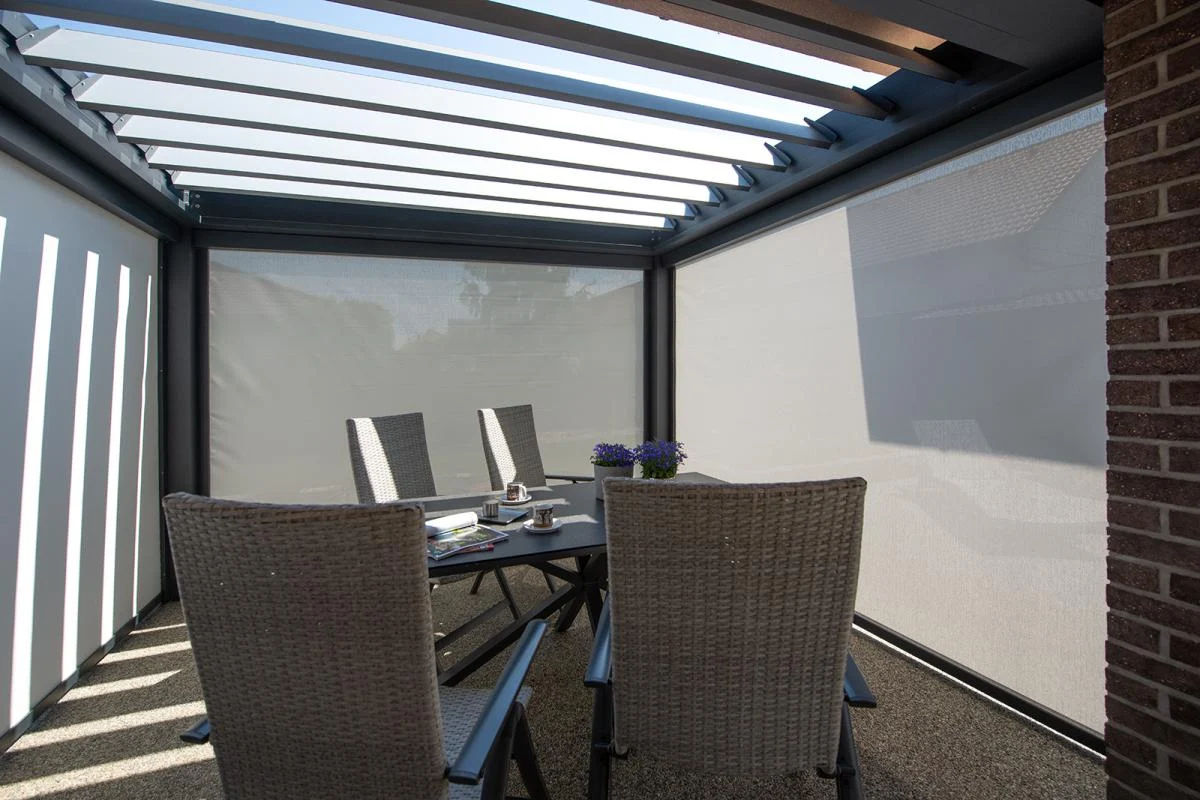 Vier Terrassenstühle und ein Tisch unter einer glasüberdachten Pergola, durch die Licht fällt. Vier Terrassenstühle und ein Tisch unter einer glasüberdachten Pergola, durch die Licht fällt.