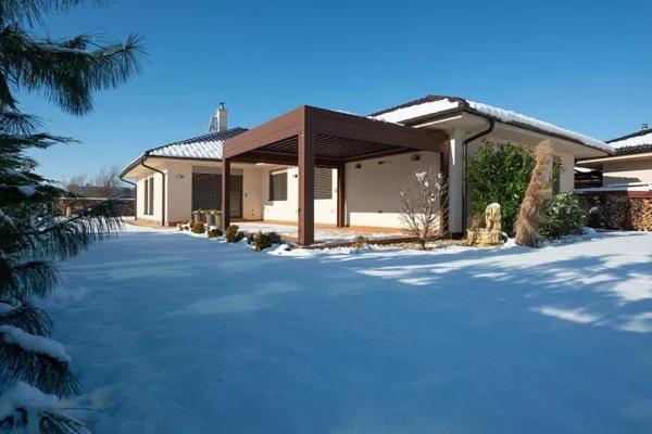 Modernes Haus mit verschneitem Hof, blauem Himmel, Pergola - perfekt für die Wintervorbereitung.