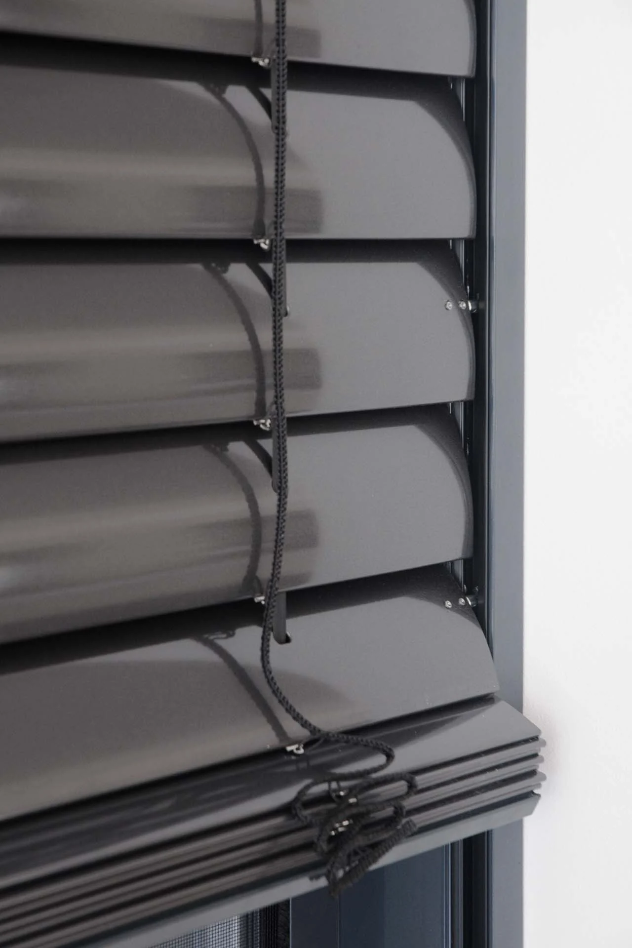 Nahaufnahme von teilweise geöffneten dunklen Jalousien mit herunterhängenden Schnüren. Nahaufnahme von teilweise geöffneten dunklen Jalousien mit herunterhängenden Schnüren.