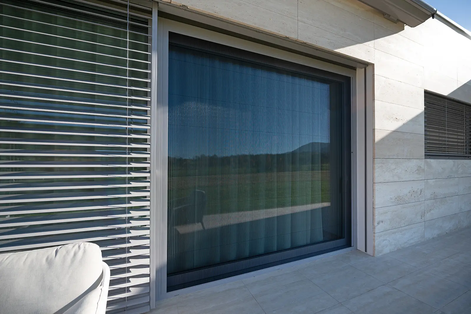 Große Glasschiebetür mit transparenten Vorhängen und Plissee, Terrasse von außen sichtbar.