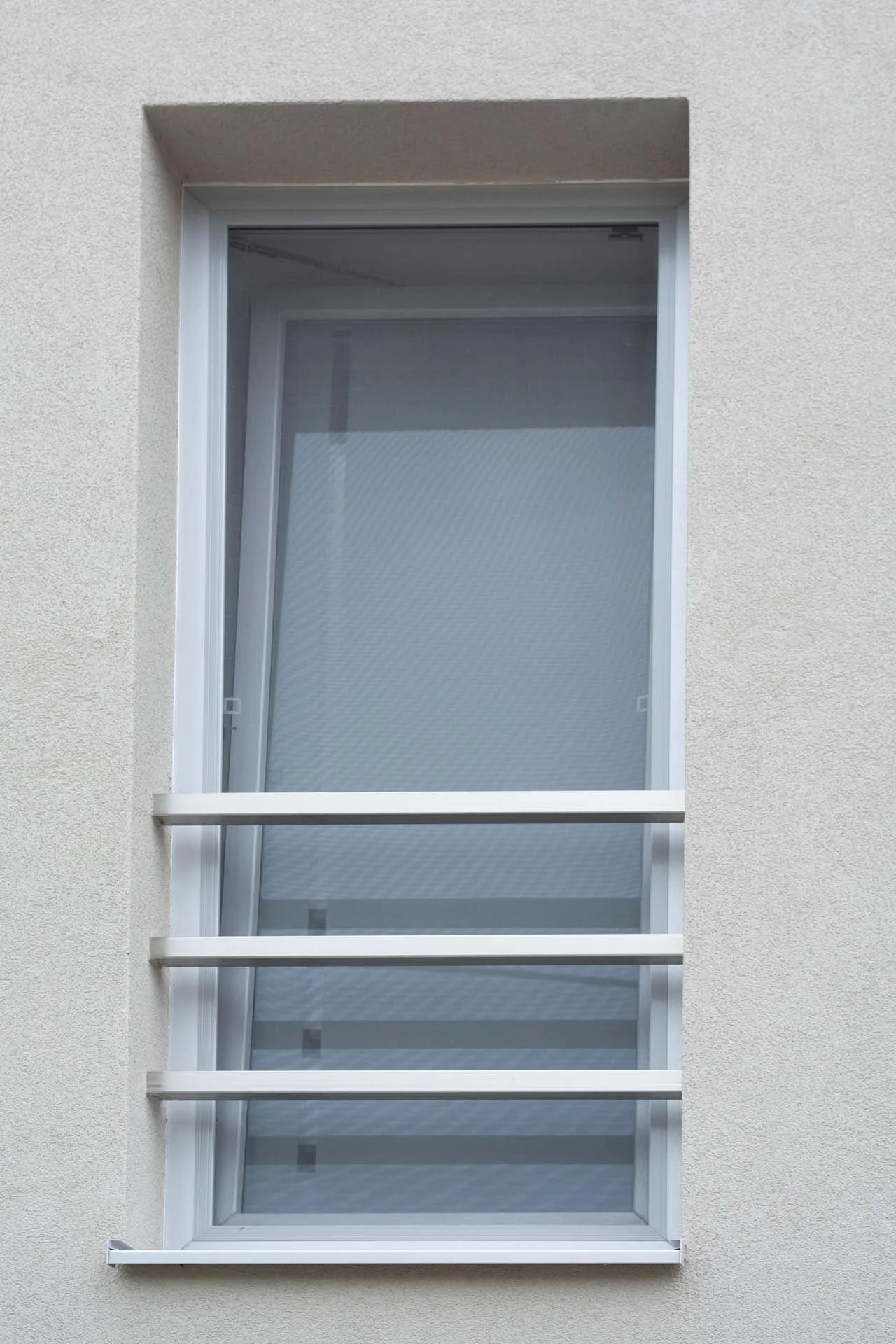 Ein gekipptes Fenster mit Metallstäben an einer schlichten hellen Wand. Ein gekipptes Fenster mit Metallstäben an einer schlichten hellen Wand.