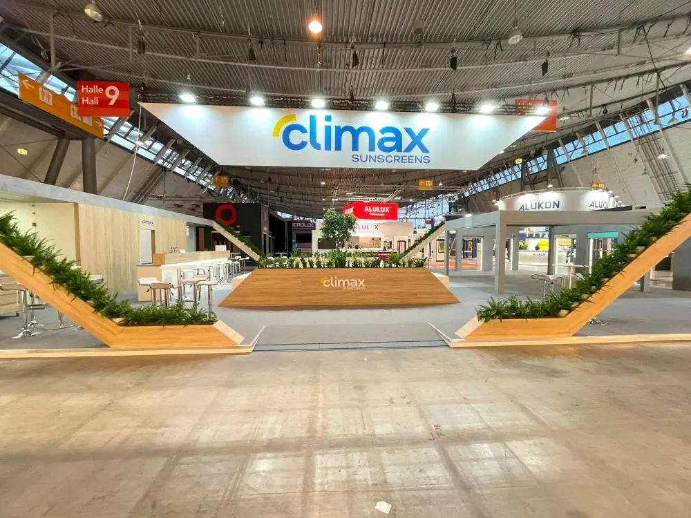 Moderner Messestand auf der R+T-Messe Stuttgart mit climax Sunscreens-Schild, Pflanzen und Sitzecke.