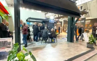 Messestand mit einer großen schwarzen Markise, unter der Menschen versammelt sind.