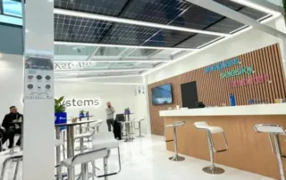 Moderner Messestand mit Sonnenkollektoren an der Decke und Tischen mit Hockern darunter.