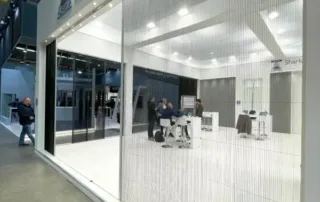 Moderner Messestand mit Menschen, die sich im Inneren unterhalten, und dünnen vertikalen Schnüren als Trennwand.