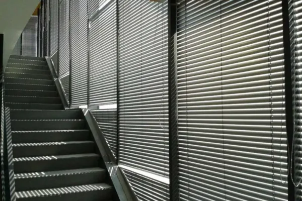 Das Sonnenlicht fällt durch die Jalousien neben einer Treppe und wirft gestreifte Schatten.